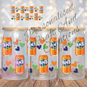 May include: Three clear glass beverage cups with wooden lids, each featuring a Fanta orange soda can design. The cups have glass straws and are decorated with orange, green, and blue hearts. The text "Personalised Craft And Creations By Sarah" is also visible.