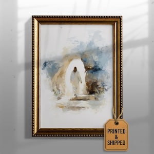 May include: Framed art print depicting a figure in white walking towards light within an archway. The artwork features a soft color palette of blues, beige, and white. The frame is gold with a textured border. A tag that says "PRINTED & SHIPPED" is attached.