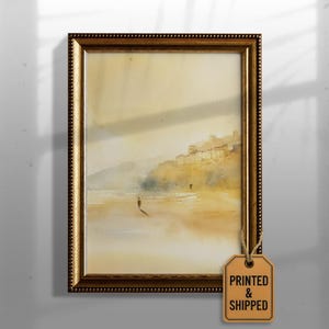 Op de afbeelding: Een ingelijste aquarel landschapsschilderij met een goudkleurige sierlijke lijst. Het kunstwerk toont een strandscène met figuren, een kustlijn en gebouwen in de verte. Het label dat aan de lijst is bevestigd, luidt "PRINTED & SHIPPED".