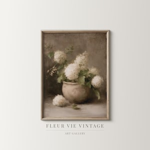 Op de afbeelding: Een ingelijst schilderij in vintage-stijl toont een stilleven van witte hortensia's in een beige keramische pot. Het kunstwerk heeft een gedempt kleurenpalet met zachte belichting en de tekst "FLEUR VIE VINTAGE ART GALLERY" staat onderaan.