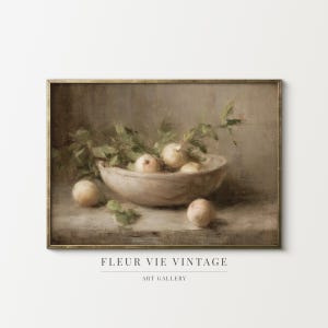 May include: A vintage still life painting depicting a wooden bowl filled with pale yellow fruit and green foliage. The artwork has a muted colour palette and a gold-toned frame. The text "FLEUR VIE VINTAGE ART GALLERY" is at the bottom.
