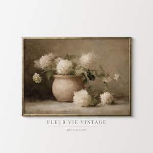 May include: A framed vintage print depicting a still life of white hydrangeas in a beige ceramic pot. The artwork has a soft, muted colour palette. The text "FLEUR VIE VINTAGE ART GALLERY" is at the bottom.