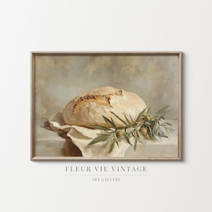 May include: A framed vintage still life painting featuring a loaf of bread on a white cloth, adorned with olive branches. The artwork has a neutral color palette with the text "FLEUR VIE VINTAGE ART GALLERY" at the bottom.