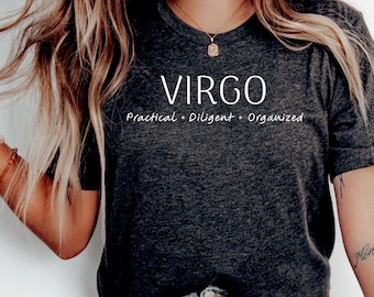 Può includere: Una maglietta grigio scuro con la parola "VIRGO" stampata in bianco sul davanti. Il testo "Practical - Diligent - Organized" è stampato sotto la parola "VIRGO".