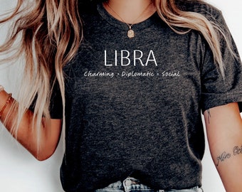 May include: A dark gray t-shirt with the word "LIBRA" printed in white on the front. The text "Charming - Diplomatic - Social" is printed below the word "LIBRA".