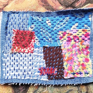 Könnte beinhalten: Ein Denim-Patch mit verschiedenen Stoffquadraten, die zusammengenäht sind. Die Quadrate weisen verschiedene Muster und Farben auf, darunter rote Kreuzstiche, blaue Blätterdrucke und florale Designs. Die Kanten sind ausgefranst.