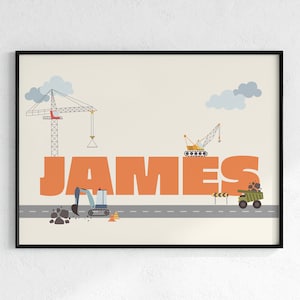 May include: A framed print featuring the name "JAMES" in large orange letters. The artwork includes illustrations of construction vehicles like a crane, excavator, and dump truck, set against a light beige background with a road.