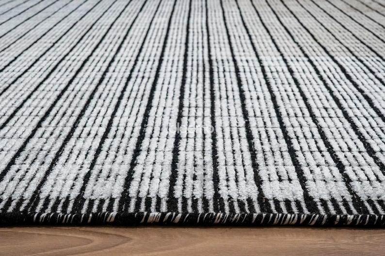 May include: A black and white striped rug with a textured surface. The rug features vertical black stripes against a white background. The rug is made of a soft material and is suitable for a living room or bedroom.