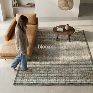 May include: A modern living room scene featuring a tan leather chaise lounge, a round wooden coffee table, and a rectangular rug with a striped pattern. The rug has a neutral color palette with the word "bloomo" on it.