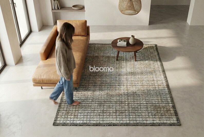 May include: A modern living room scene featuring a tan leather chaise lounge, a round wooden coffee table, and a rectangular rug with a striped pattern. The rug has a neutral color palette with the word "bloomo" on it.
