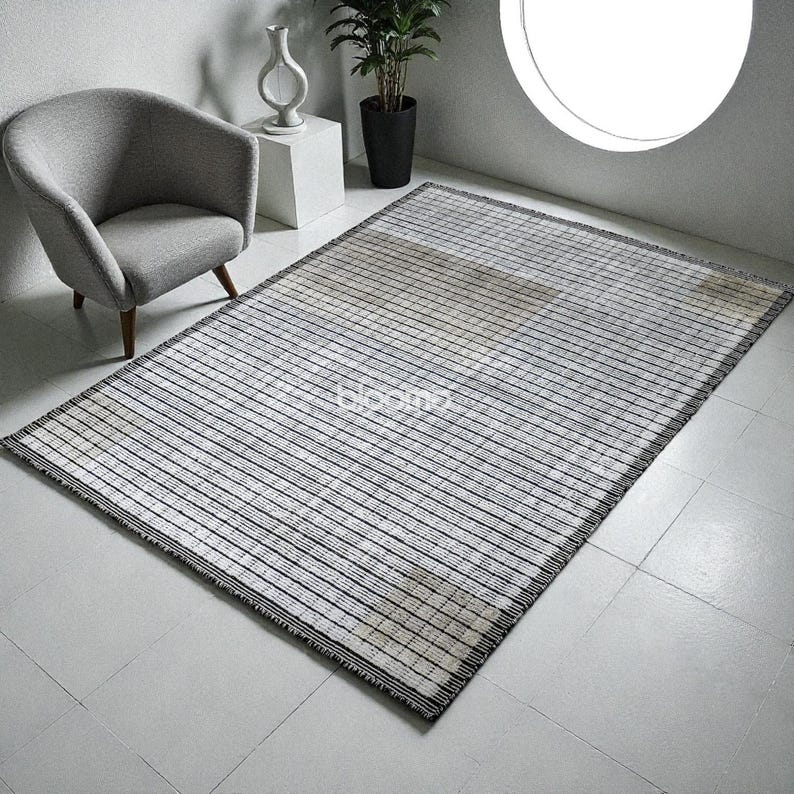 May include: A rectangular rug with a striped pattern in shades of white, gray, and black. The rug has a woven texture and a dark border. The design features horizontal lines across the surface, creating a modern aesthetic. The rug is suitable for living rooms and bedrooms.