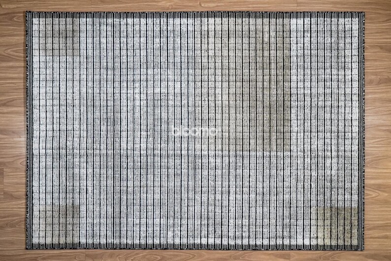 May include: Rectangular rug with a vertical striped pattern in shades of gray and black. The rug has a textured appearance and a dark border. The rug is placed on a wooden floor.