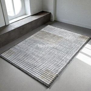May include: Rectangular rug with a striped pattern in black and white. The rug has a fringe on the edges and is placed on a gray floor. The word "bloomco" is visible on the rug.