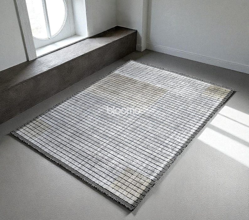 May include: Rectangular rug with a striped pattern in black and white. The rug has a fringe on the edges and is placed on a gray floor. The word "bloomco" is visible on the rug.