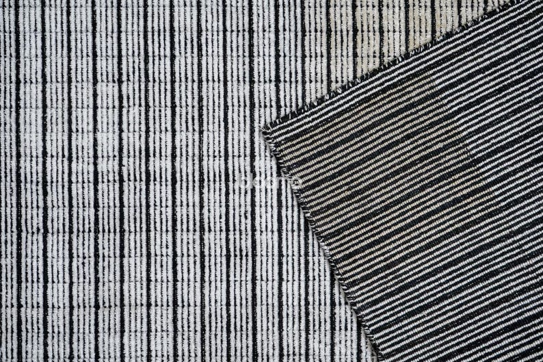 May include: Close-up of a textured fabric with a black and white striped pattern. The fabric is divided into two sections, one with vertical stripes and the other with diagonal stripes. The design is simple and modern, suitable for home decor.