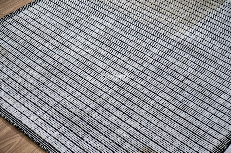 May include: A rectangular rug with a striped pattern. The rug features alternating black and off-white stripes running diagonally across the surface. The rug is made of a woven material and has a dark border.