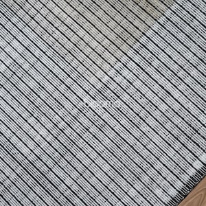 May include: Close-up of a textured rug with a diagonal striped pattern in black and white. The rug's corner is visible, resting on a wooden floor.