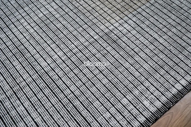 May include: A black and white striped rug with a textured surface. The rug features a pattern of diagonal lines, creating a modern and minimalist design. The rug is made of a durable material and is suitable for high-traffic areas.