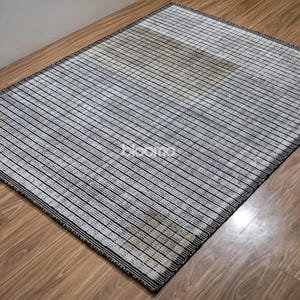 May include: Rectangular rug with a striped pattern in black and white. The rug has a black border and is placed on a wooden floor. The word "bloomo" is visible on the rug.