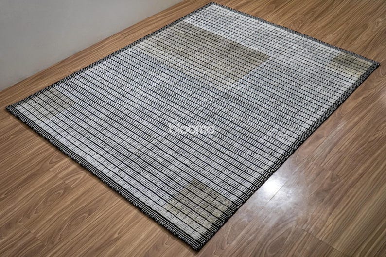 May include: Rectangular rug with a striped pattern in black and white. The rug has a black border and is placed on a wooden floor. The word "bloomo" is visible on the rug.