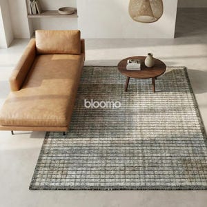 May include: An overhead shot of a modern living room with a tan leather chaise lounge, a small round wooden coffee table, and a rectangular rug with a striped pattern. A small vase and books are on the table.