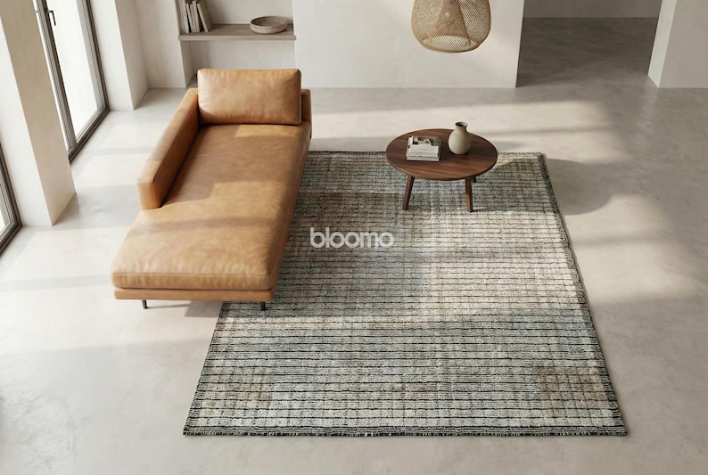 May include: An overhead shot of a modern living room with a tan leather chaise lounge, a small round wooden coffee table, and a rectangular rug with a striped pattern. A small vase and books are on the table.