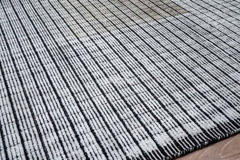 May include: A black and white striped rug with a textured surface. The rug features vertical stripes, creating a pattern across the surface. The rug is made of a woven material.