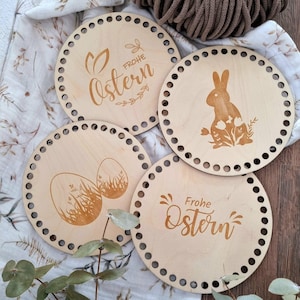 Könnte beinhalten: Vier runde Holzornamente mit einem Loch am Rand. Jedes Ornament hat ein anderes Osterdesign, darunter ein Hase, Eier und der Text "Frohe Ostern".