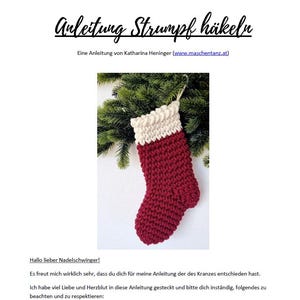 May include: A burgundy red knitted Christmas stocking with a cream-coloured cuff, displayed against a backdrop of green pine branches. The image includes German text at the top and bottom.