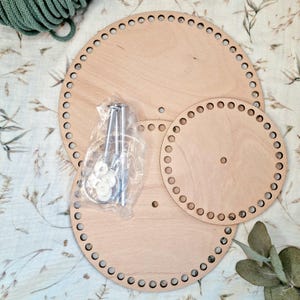 Può includere: Due telai circolari in legno con fori attorno ai bordi. Il telaio più grande ha un diametro di 30 cm e quello più piccolo ha un diametro di 20 cm. Un pacchetto di ferri da maglia in metallo e rondelle si trova al centro dell'immagine.