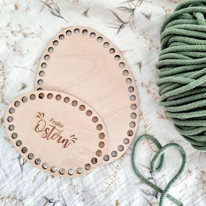 Könnte beinhalten: Zwei ovale Holz-Webringe mit Löchern an den Rändern. Der kleinere Ring hat den Text "Frohe Ostern" eingraviert. Im Hintergrund befindet sich ein grünes Seil.