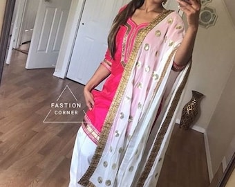 May include: A woman wearing a pink and gold salwar kameez with a white dupatta. The dupatta has gold embroidery and sequins. The woman is standing in front of a mirror and taking a selfie.