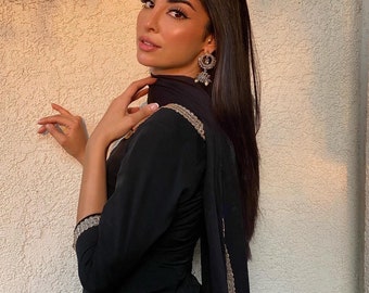 May include: A woman wearing a black salwar kameez, a traditional South Asian outfit. The outfit features gold embroidery on the sleeves and edges of the dupatta. She is also wearing silver earrings.