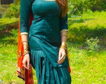 May include: A woman wearing a teal salwar kameez with gold trim and matching pants. She is wearing a red and gold dupatta and gold jewelry. The image has the text "FASHION CORNER".