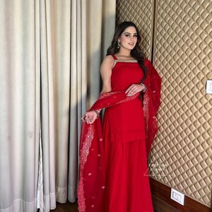 Op de afbeelding: Een vrouw draagt een rode salwar kameez met een bijpassende rode dupatta. De dupatta heeft een zilveren en witte geborduurde rand. De outfit is een traditionele Indiase kleding.