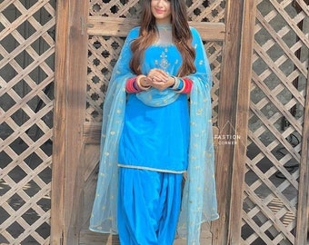 May include: A bright blue salwar kameez set featuring a sleeveless tunic with silver embroidery at the neckline, matching pleated trousers, and a sheer, light blue dupatta with gold floral accents. The outfit includes red and blue bangles.