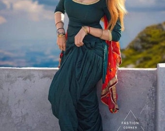 May include: A dark teal salwar kameez ensemble with a matching dupatta. The outfit features gold trim and jewelry, including bracelets and anklets. The image includes the text "FASHION CORNER".