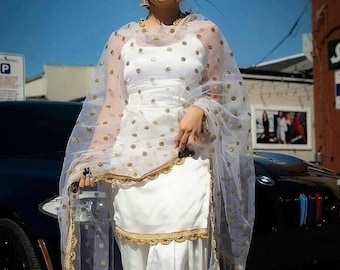 May include: A white salwar kameez with gold polka dots and a matching sheer dupatta. The outfit features a gold trim and a tassel detail. The text "FASTION CORNER" is visible in the bottom right corner of the image.