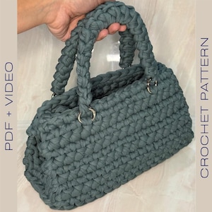 Pode incluir: Uma bolsa de mão de crochê azul-esverdeada com duas alças e argolas prateadas.  PDF + VIDEO. CROCHET PATTERN.