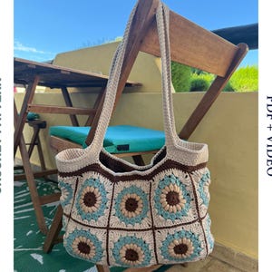 以下が含まれることがあります： ベージュ、ブラウン、ティール色の花柄が特徴的な手編みのトートバッグ。長い持ち手があり、木製の椅子とテーブルを背景に展示されています。「CROCHET PATTERN」と「PDF + VIDEO」の文字が見えます。