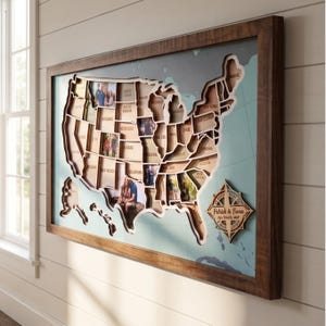 May include: A wooden framed wall map of the United States featuring laser-cut state outlines layered over a light blue background. Several states contain personal photographs. A wooden compass rose ornament displays the text Patrick & Fiona USA Travel Map.
