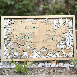 May include: A rectangular wooden wall map of the United States featuring laser-cut state outlines and national park locations marked with small tree icons. The map includes a decorative border with hiker silhouettes and a plaque reading Amy & William Travel Map.