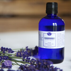May include: A blue glass bottle with a white label that reads "Lavender Lavandula Angustifolia Pure Essential Oil (100ml)" and "www.auroessentialoils.co.uk". The bottle is surrounded by lavender flowers.