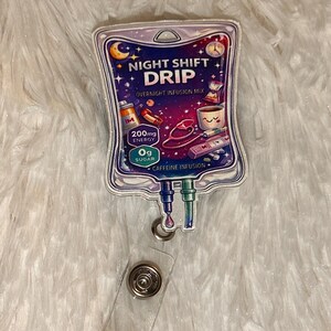 May include: A badge reel with a design resembling an IV bag, featuring the text "NIGHT SHIFT DRIP" and "OVERNIGHT INFUSION MIX." The design includes illustrations of a coffee cup, pills, and a stethoscope, with the text "200mg ENERGY" and "0g SUGAR."