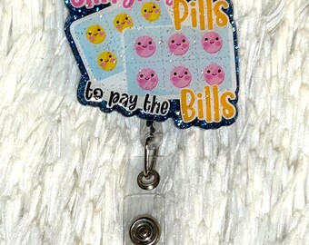 May include: A blue glitter badge holder with a pink and yellow pill design. The text on the badge holder reads "Slinging Pills to pay the Bills".