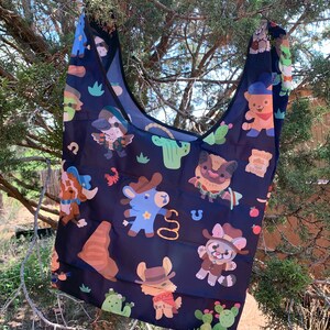 May include: A black reusable tote bag with a colorful pattern of cartoon animals wearing cowboy hats and riding horses. The pattern also includes cacti and other western-themed imagery.