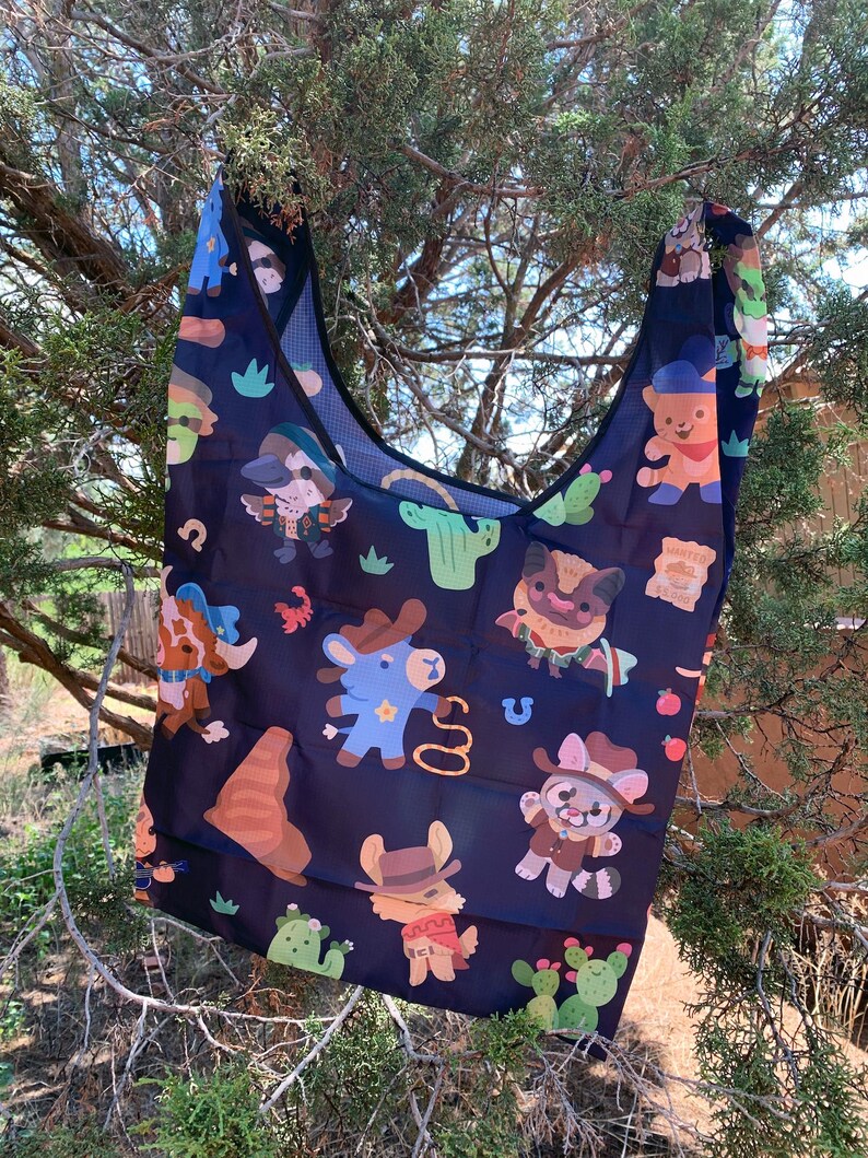 May include: A black reusable tote bag with a colorful pattern of cartoon animals wearing cowboy hats and riding horses. The pattern also includes cacti and other western-themed imagery.