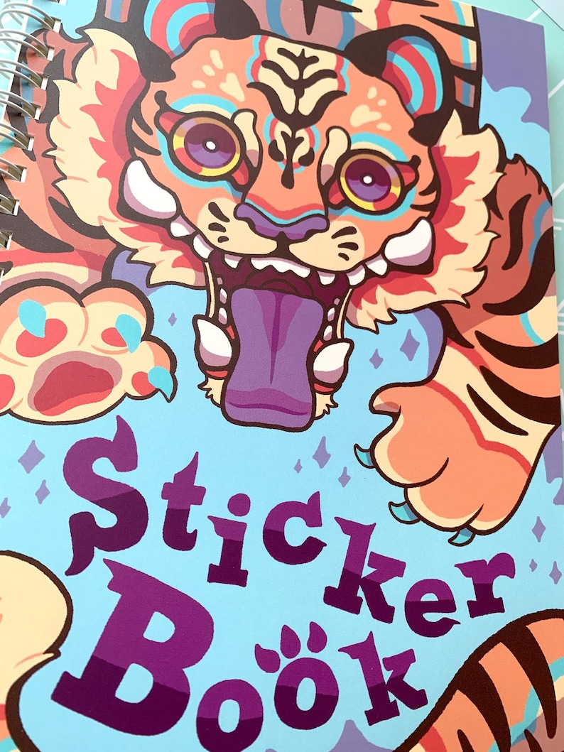 May include: A blue and purple sticker book with a colorful cartoon tiger on the cover. The tiger has orange, red, and blue stripes and bright yellow eyes. The text "Sticker Book" is in a purple font.