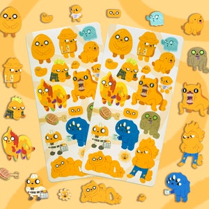 May include: A set of 24 colorful cartoon stickers featuring a variety of characters, including a dog, a ghost, and a creature with a large mouth. The stickers are on a yellow background with a wavy pattern.