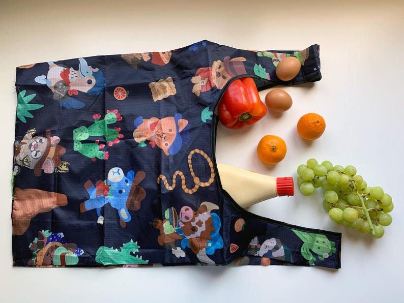 May include: A black reusable shopping bag with a colorful cartoon print of animals and plants. The bag is filled with groceries, including a red pepper, oranges, grapes, and a bottle of mayonnaise.